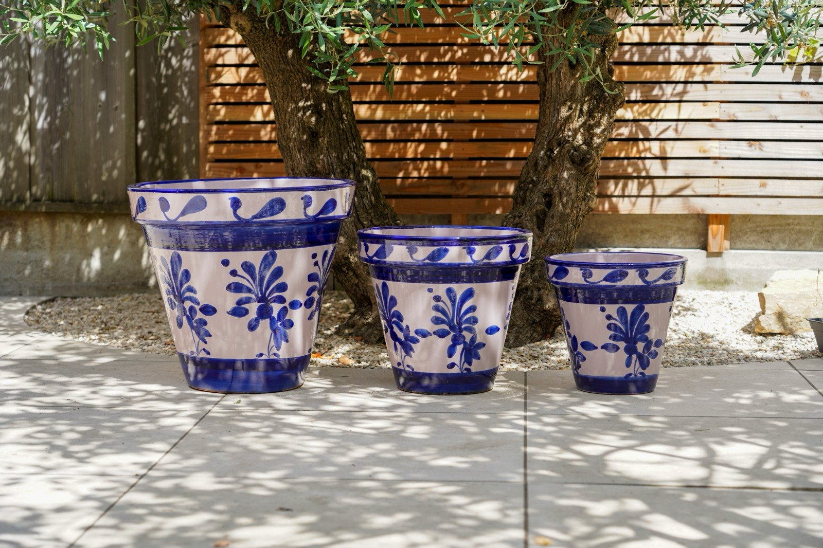 Drie Spaanse keramieken bloempotten in blauw-wit onder een olijfboom